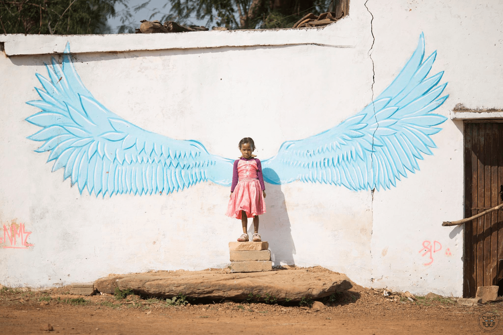 A little girl standing in front of a wall with painted wings