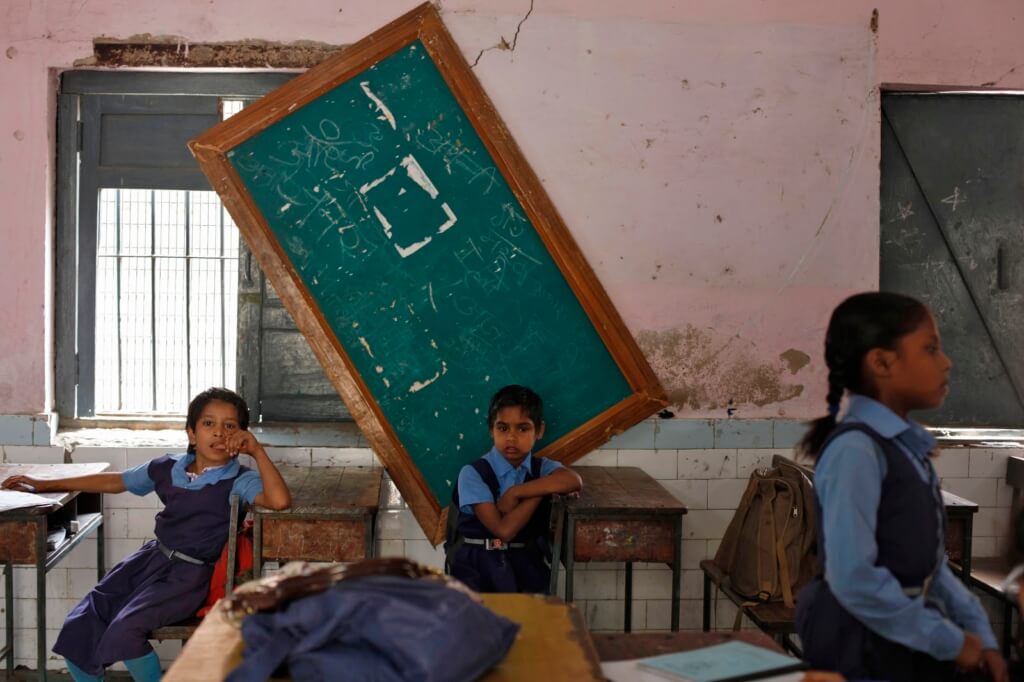 Children studying in a classroom with the board fallen down in the background